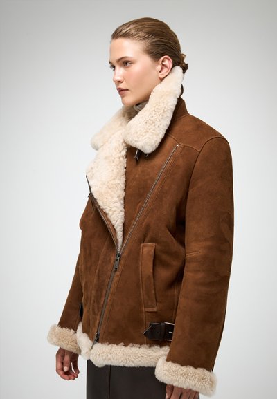 Brun ruskind shearling-jakke med en fuzzy beige krave og manchetter, skrå lynlås, og justerbar spænde detalje i taljen.