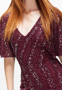 Bordeauxfarbiges Kurzarmkleid mit V-Ausschnitt, verziert mit Pailletten in einem diagonalen Muster, das die Textur und die feinen Details betont.