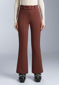 Hnedé rozšírené nohavice s opaskom vysokého pásu, s výraznými švovými detailmi a hladkým povrchom. Čierne topánky so striebornými akcentmi.