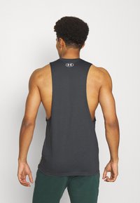 Camiseta de gimnasio sin mangas de color gris oscuro con una gran abertura en la espalda y detalle del logo en el cuello. Textura suave y corte holgado.