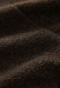 Tissu brun texturé avec une surface douce et duveteuse et un léger éclat. Le matériau présente une couleur riche et profonde avec des fibres visibles et un motif ondulé délicat.