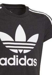 Svart t-shirt i bomull med korta ärmar, med en stor vit Adidas-logotyp och tre vita ränder på varje axel.