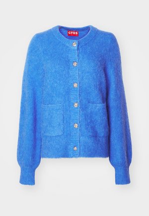 Zila vilnas kardigāna ar noapaļotu kakla izgriezumu, garām pūkainām piedurknēm, divām priekšējām kabatām un dekoratīvām sudraba pogām gar plāksni.