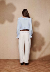Blouse bleu clair courte avec manches bouffantes et ourlet à volants, associée à un pantalon blanc à jambes larges. Le dos présente un design simple sans motifs.