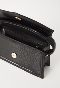 Sac à main noir en simili cuir texturé avec un motif crocodile. Dispose d'une fermeture rabat et d'un détail bouton doré. Comprend une petite poche zippée.