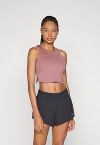 Rozā īsā sporta krekls ar apaļu apkakli un mazu logo; apvienots ar melniem skriešanas šortiem ar platām elastīgām jostasvītrām.