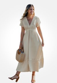 Robe en coton beige avec un décolleté en V, manches courtes, détails en dentelle à la taille et à l'ourlet. Portée avec des sandales à talons marron et un sac tissé.