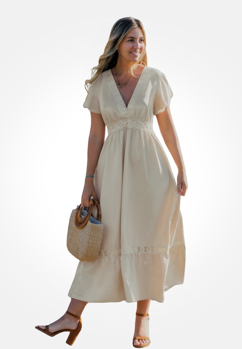 Robe en coton beige avec un décolleté en V, manches courtes, détails en dentelle à la taille et à l'ourlet. Portée avec des sandales à talons marron et un sac tissé.