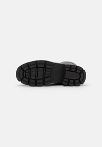 Semelle de chaussure en caoutchouc noir avec des profondeurs de crantage, une forme courbée et un emblème central. Surface texturée pour une meilleure adhérence et durabilité.