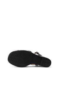 Suela negra de una sandalia con un patrón texturizado y tachuelas metálicas a lo largo del borde, vista desde abajo sobre un fondo blanco.