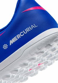 Gros plan sur une chaussure Nike Mercurial bleue montrant le swoosh rose, la semelle texturée avec des crampons, et le logo "Mercurial" sur le côté supérieur.