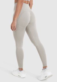Lichtbeige leggings met een gemêleerd patroon op de zijkanten, hoge taille en naadloze afwerking; gecombineerd met witte sportieve schoenen.
