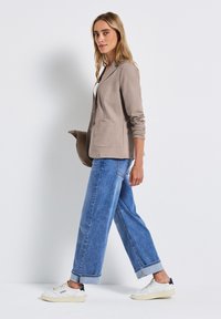 Ljusbrun kavaj med en knapp, två framfickor, kombinerad med lösa blå jeans och vita sneakers. Enkelt och avslappnat utseende.