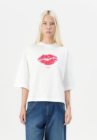 Weißes Baumwoll-T-Shirt mit einem großen roten Lippen-Print auf der Vorderseite. Das Shirt hat kurze Ärmel und eine lässige, kastige Passform.