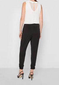 Czarny kombinezon z dopasowaną talią i luźnymi nogawkami, zestawiony z bezrękawną białą bluzką z wycięciem na plecach. Czarne szpilki.