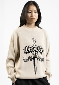 Beige gebreide trui met een zwart grafisch ontwerp van een zwaard en een banner met de tekst "Always Faithful 2012." Losse pasvorm en ribgebreide halslijn.