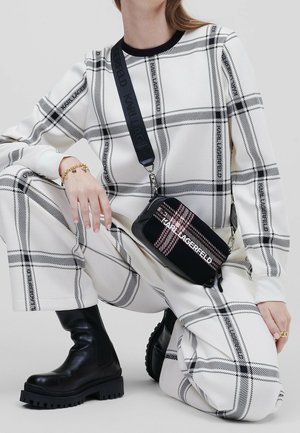 Sort-hvid ternet crossbody taske med en struktureret kanvasfinish, der har et logo, vedhæftet rem og kædedetalje.