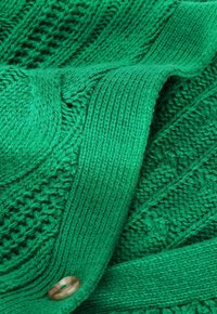Maglione verde lavorato a maglia con motivo a costine testurizzate e una sezione liscia, impreziosito da un grande bottone sul davanti.
