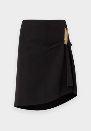 Jupe enveloppante noire avec un ourlet diagonal, texture lisse et un accent de fermoir décoratif en or sur le côté. Design simple et ajusté.