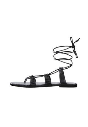 Sandales en cuir noir avec semelles plates, comprenant trois parties de lanières et un lien en spirale autour de la cheville. Texture lisse et design minimaliste.