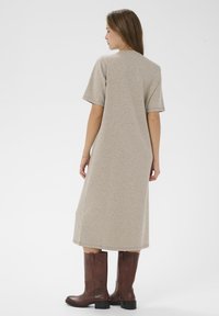 Bežs, līdz ceļgaliem garš, īsām piedurknēm tērps, izgatavots no mīkstas auduma ar brīvu krāsu, apvienots ar brūnām ādas augstām zābakiem.