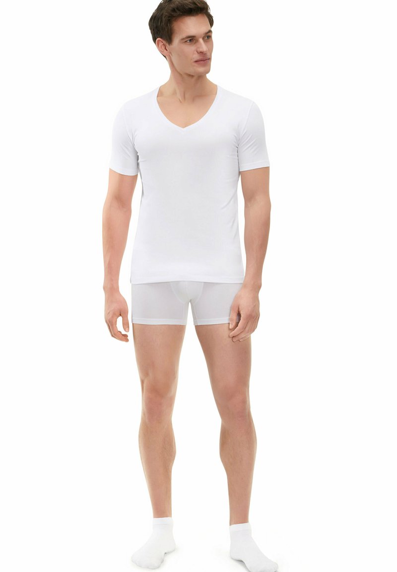 White short-sleeve v-neck t-shirt paired with white boxer briefs, both made of smooth, stretch fabric. Model wearing white ankle socks.