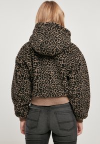 Chaqueta corta con capucha hecha de suave y texturizada piel sintética negra y marrón con un patrón de leopardo y dobladillo acanalado. Jeans negros visibles.