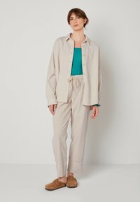 Ljusbeige korduray skjorta med knappar, turkos topp, strukturerade beiga byxor med dragsko, och bruna slip-on skor. Enkel design och avslappnad passform.