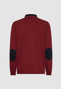 Polo a maniche lunghe color marrone con toppe sui gomiti trapuntate nere, colletto e polsini a coste. Tessuto liscio e design semplice.