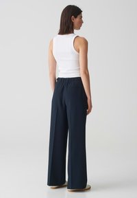 Marineblauwe wijde broek met een ontspannen pasvorm, voorzien van een elastische tailleband en twee achterzakken, gecombineerd met een witte mouwloze top.