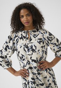 Floral-patterned dress in cream, blue, and black with puff sleeves and a keyhole neckline. Features a tie detail at the neck.