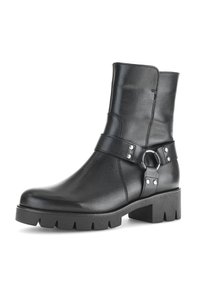 Bottine en cuir noir avec un bout arrondi, une semelle épaisse, des détails de bride à boucle et des clous en métal argenté. Texture lisse avec des coutures minimales.