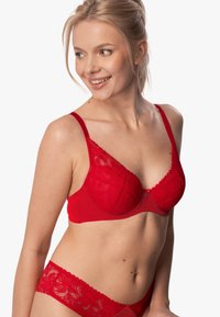 Czerwony koronkowy biustonosz z kwiatowym wzorem, siateczkowymi wstawkami, fiszbinami i regulowanymi ramiączkami. Częściowo widoczne dopasowane czerwone koronkowe figi.