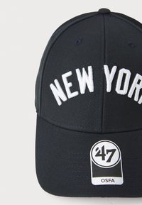 Black baseball cap with embroidered "NEW YORK" in white, structured design, adjustable strap, and logo tag reading "’47 OSFA."