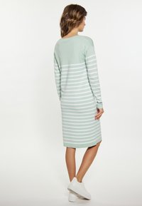 Rochie tricotată în dungi, de culoare verde mentă și albă, cu mâneci lungi, până la genunchi, cu decolteu rotund și croială lejeră. Asortată cu adidași albi.