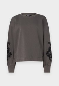 Felpa grigia con maniche lunghe, scollatura rotonda, polsini elastici e ricami ornamentali neri sulle maniche. Tessuto dalla texture liscia.