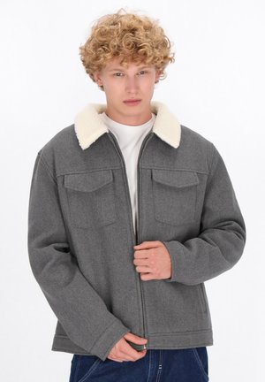 Gray fleece jacket with a fluffy white collar, zip closure, two chest pockets, and a relaxed fit. Worn over a white shirt.