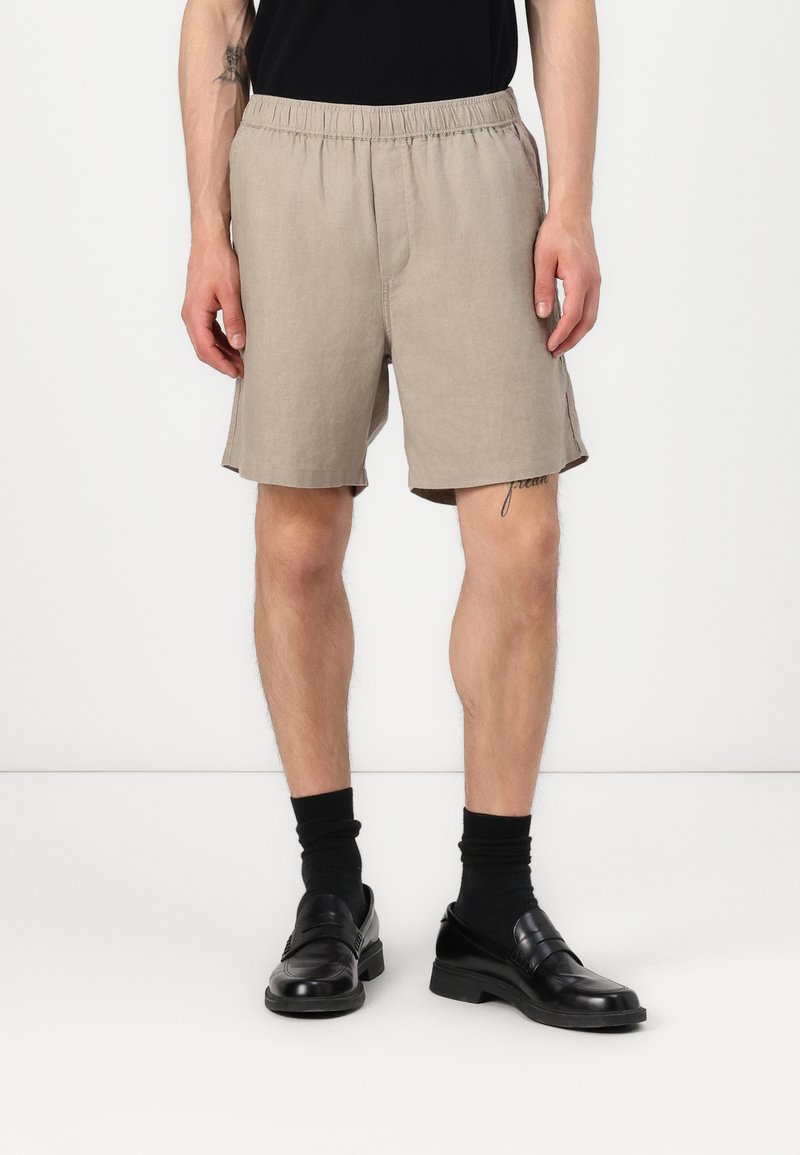 Beige linnen shorts met een elastische tailleband, zijzakken en een relaxed fit. Draag ze met zwarte sokken en instappers.