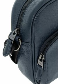 Ciemnoniebieska skórzana torba z dwoma zamykanymi na zamek przegrodami, z ozdobnymi srebrnymi elementami i teksturowanym wykończeniem. Miękkie krawędzie i trwała konstrukcja.
