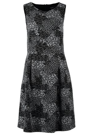 Woman wearing sleeveless black and gray animal print dress, black tights, ankle boots, holding beige clutch bag at side.