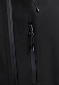 Tissu de veste noir avec une poche zippée verticale étanche avec doubles tirettes à cordon et un cordon noir réglable avec stoppeur.