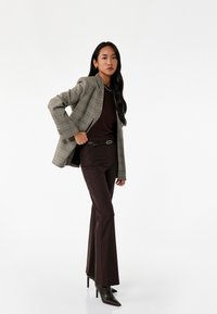 Grå ternet blazer over en brun top, parret med brune flagrende bukser og sorte høje støvler; har en slank pasform og skræddersyet design.