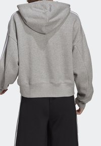 Grå kort hoodie med huva, som har vita sidostreck, sänkta axlar och ribbade muddiga ärmar, tillverkad av mjukt material.