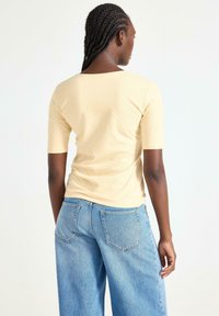 Kortærmet, gul top lavet af blødt materiale, parret med lyseblå, brede jeans med baglommer og en afslappet pasform.