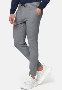 Graue, schmal zulaufende Hose mit Kordelzugbund, zwei Seitentaschen und strukturierter Stoff, kombiniert mit weißen Sportschuhen.