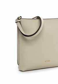 Borsa a mano in pelle beige con una texture liscia, caratterizzata da una finitura nera e un logo dorato. È dotata di una singola tracolla regolabile per il trasporto.