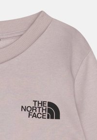 Világos rózsaszín pulóver, puha anyagból készült, bal felső sarokban a "The North Face" fekete logójával. Bordázott nyakrészes részlet.