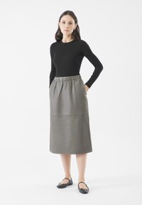 Grau lederne Midi-Rock mit elastischem Bund, Seitentaschen und glatter Textur. Kombiniert mit einem schwarzen Langarmshirt und schwarzen Ballerinas.