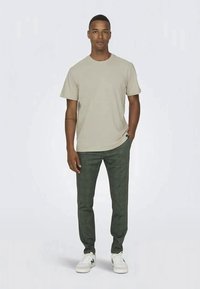 Beige cotton t-shirt with short sleeves, paired with dark green plaid trousers and white sneakers with gray accents.