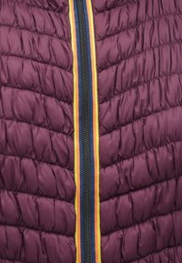 Μπορντό κουβερτίνα με φερμουάρ στην μπροστινή πλευρά, που διαθέτει κίτρινες, πορτοκαλιές και ναυτικές ρίγες κατά μήκος της γραμμής του φερμουάρ.